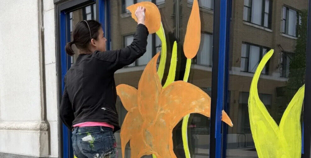Kelly Witte painting her floral window art display for the Makers' Gallery